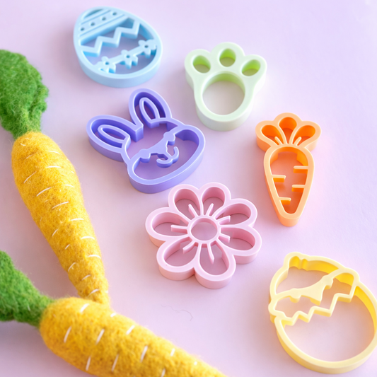 Set of colorful cookie cutters shaped like vegetables and animals on a light pink background