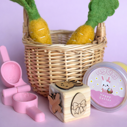 Wicker basket with pineapple-shaped toys, pink sand toys, wooden block, and Easter-themed container on a light purple background.